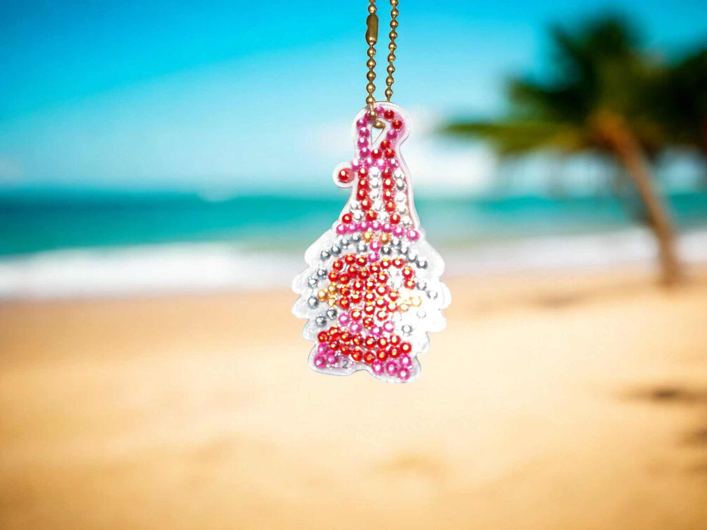 Pink and red gnome keychain with beads hanging outdoors near beach background