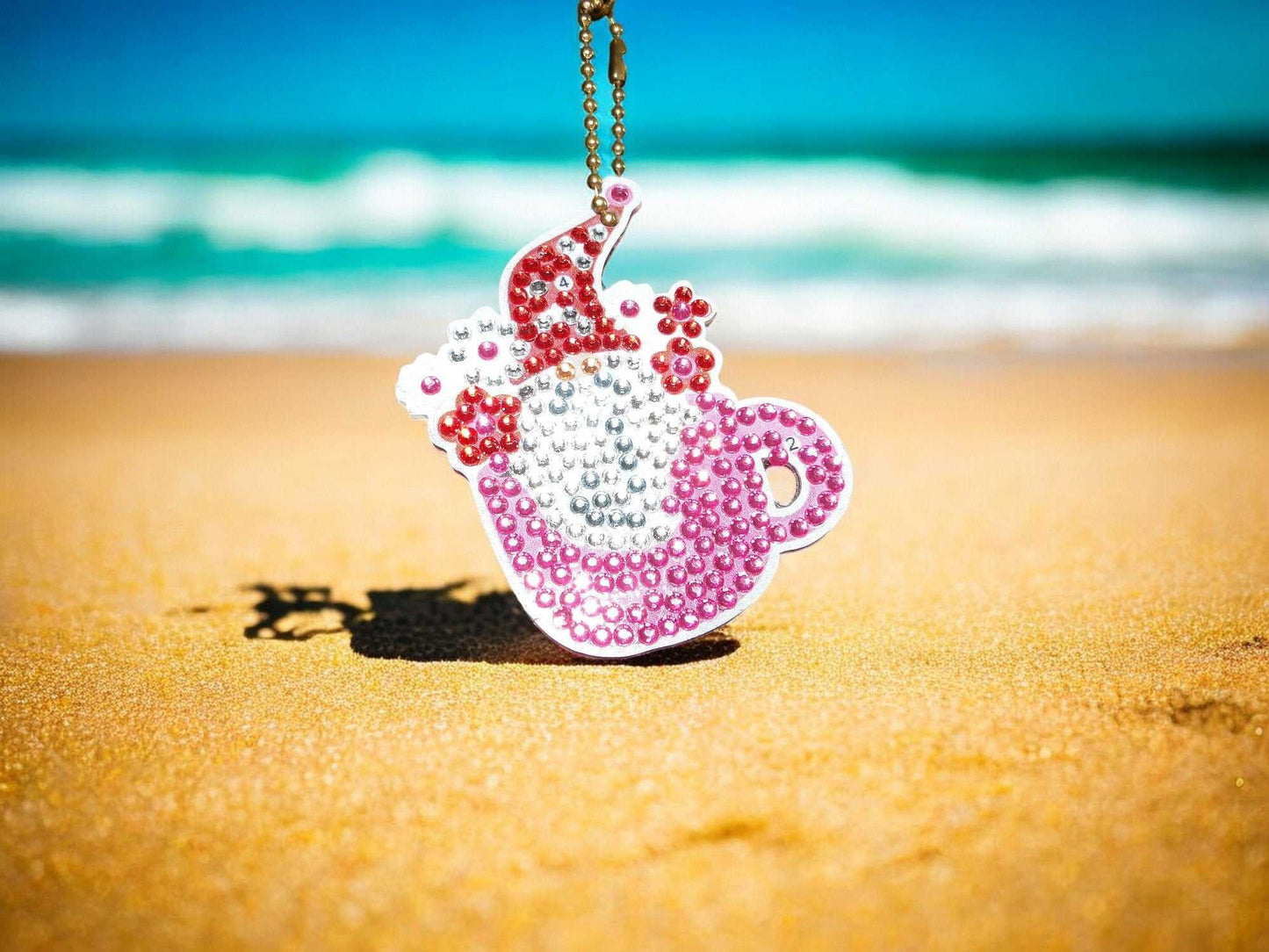 Pink teapot gnome keychain with rhinestones hanging on beach background