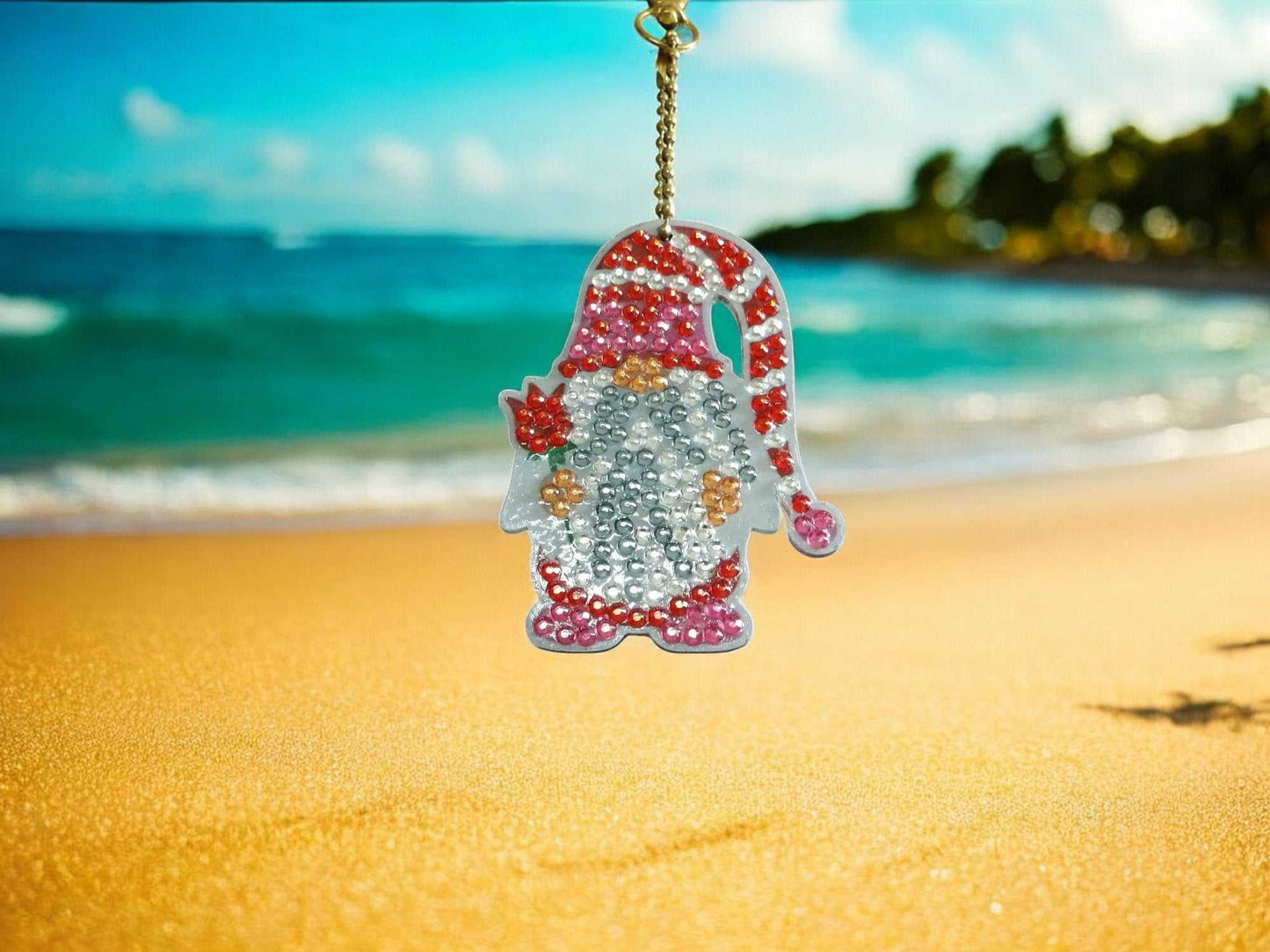 Santa Gnome Keychain with rhinestones hanging on a gold chain on a beach background
