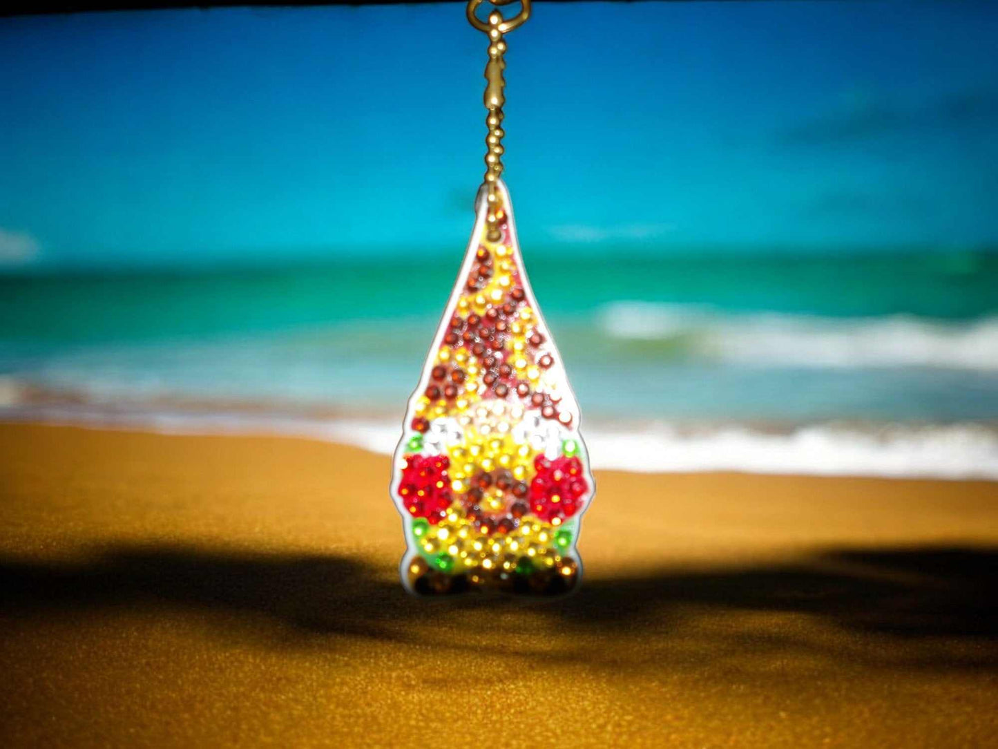 Brown hat gnome keychain with colorful beads hanging on beach background
