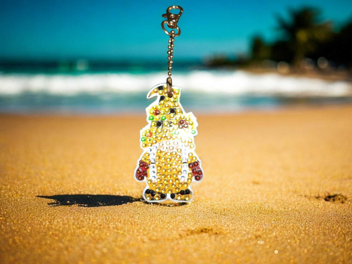 Golden Gnome Keychain with colorful beads on sandy beach background