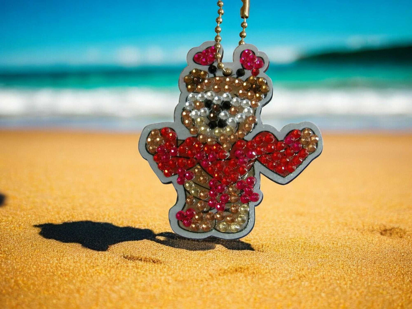 Teddy Bear Bringing Love keychain with colorful beads on sandy beach background