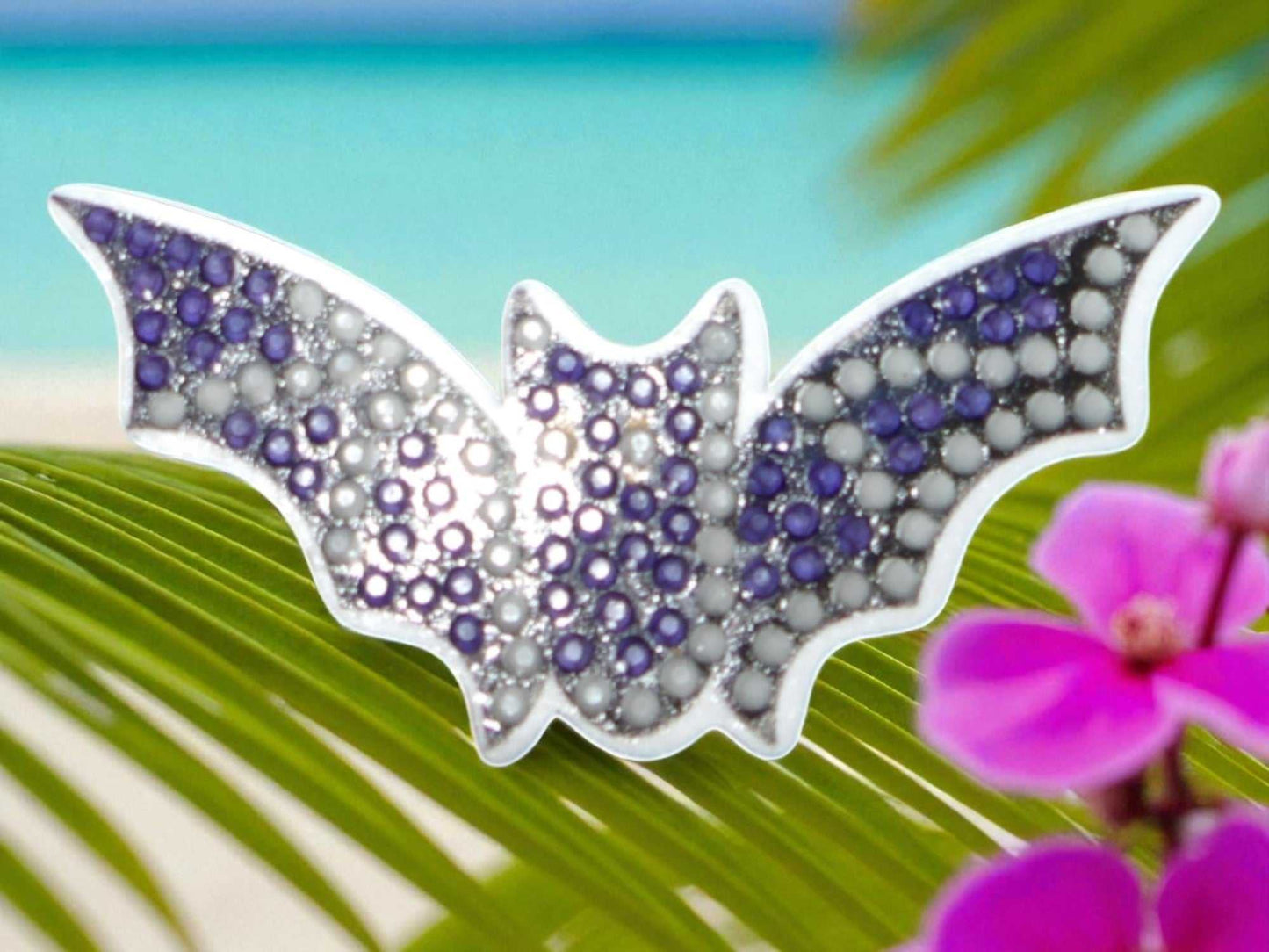 Glow in the dark flying bat magnet with purple and white beads on tropical background