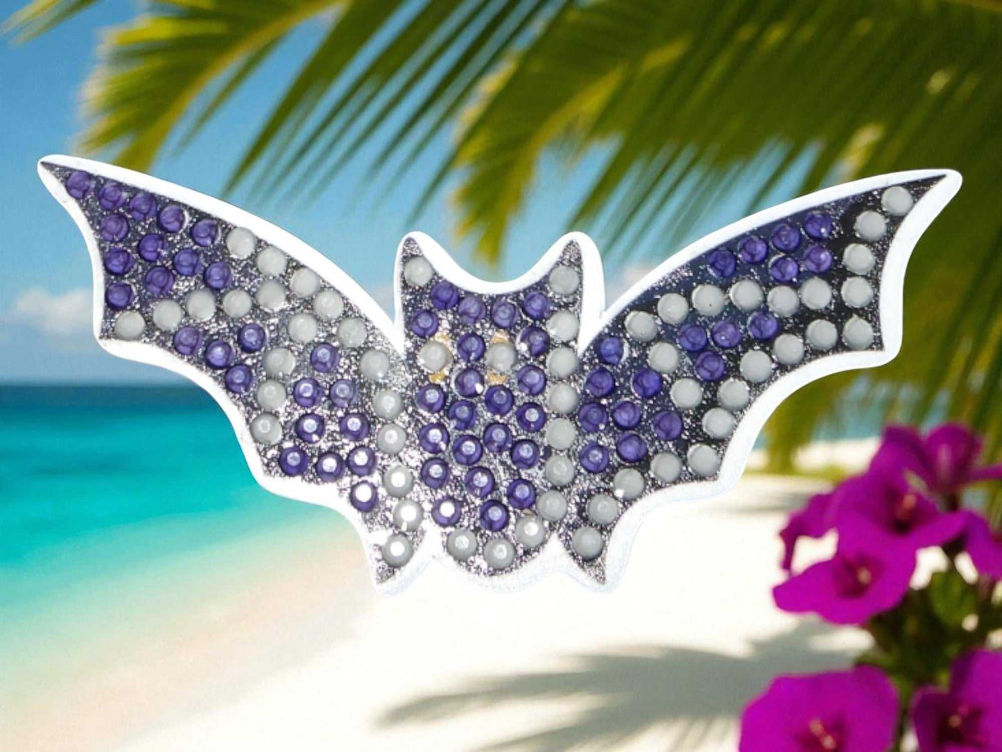 Glow in the dark flying bat magnet with purple and white beads on beach background