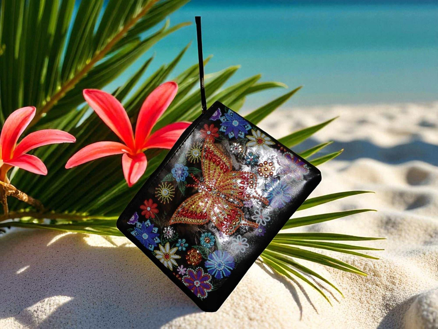 Golden Butterfly Large Hand Clutch with decorative butterfly and floral design placed on sand with tropical flowers and palm leaves background