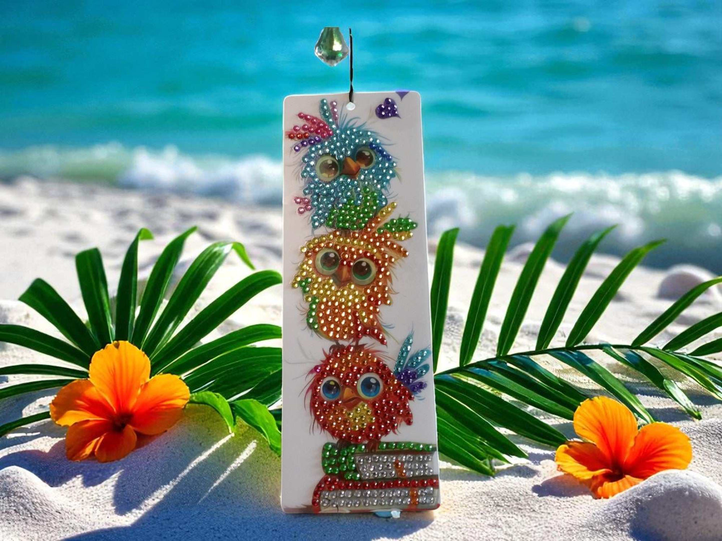 Playful colorful birds bookmark with vibrant bird illustrations on a white background, displayed on sand with tropical leaves and flowers.