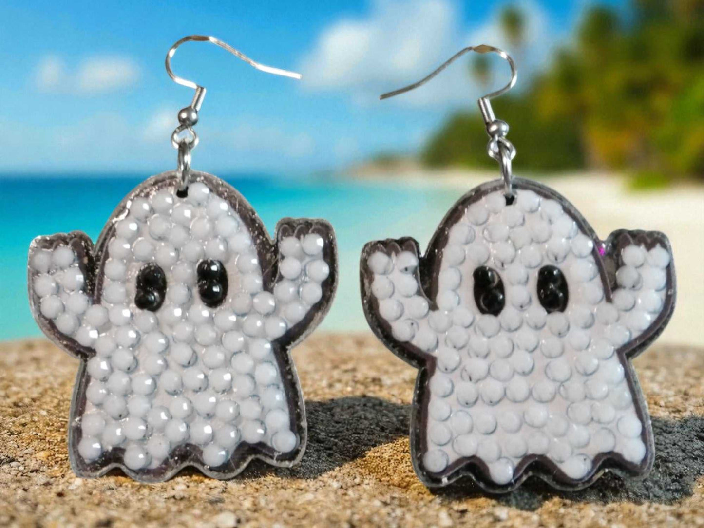 Glow in the dark ghost earrings with bead details on sandy beach background