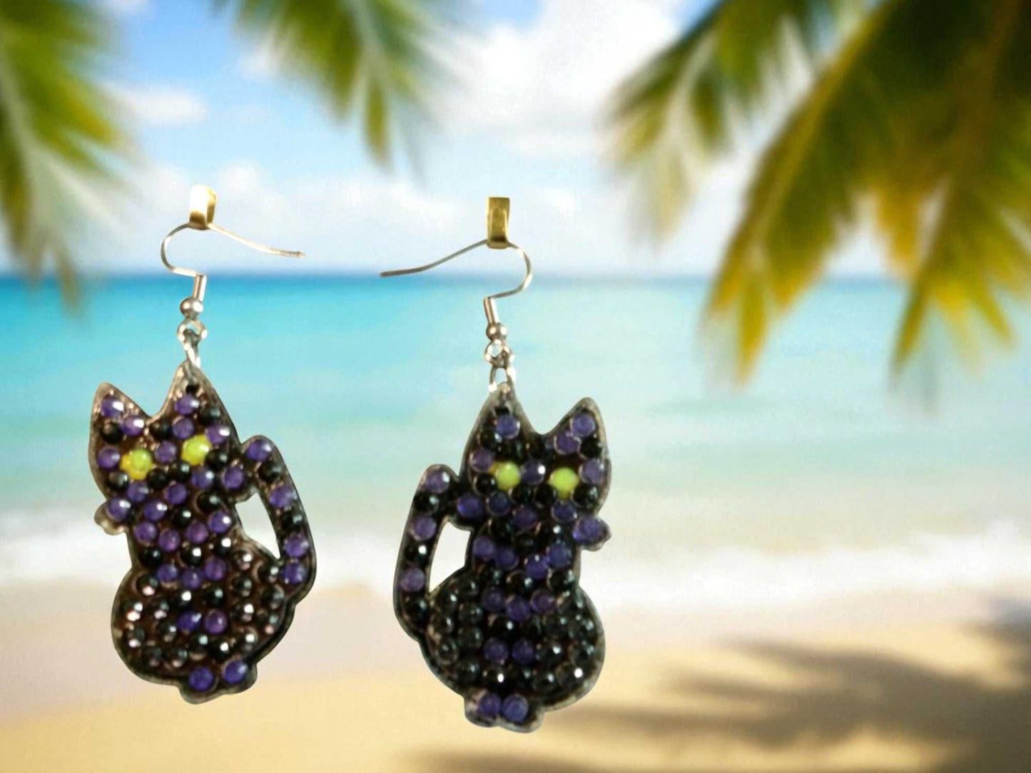 glow in the dark black cat earrings with colorful beads hanging by the beach background