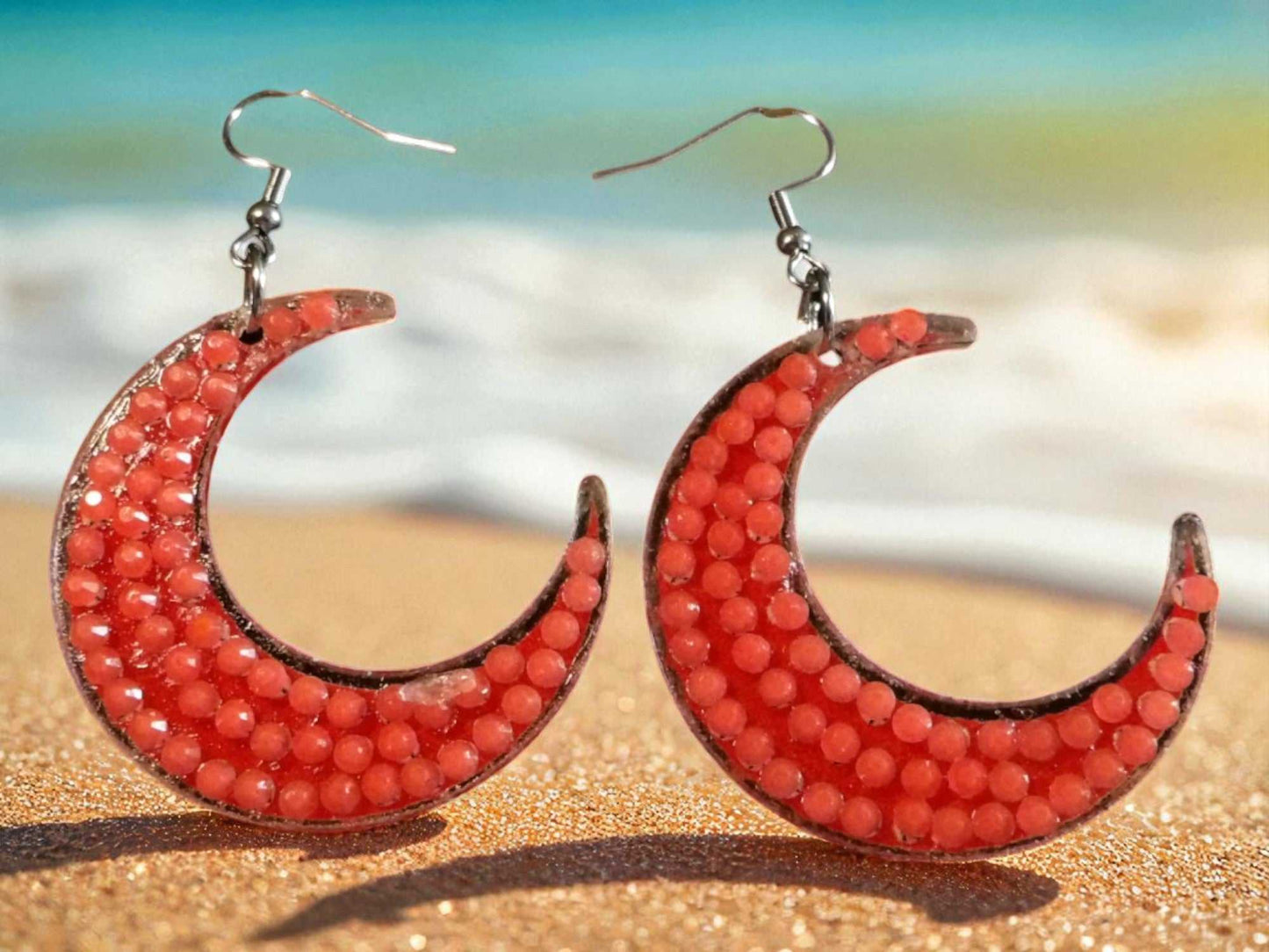 Glow in the dark half moon earrings with red beads on sandy beach background