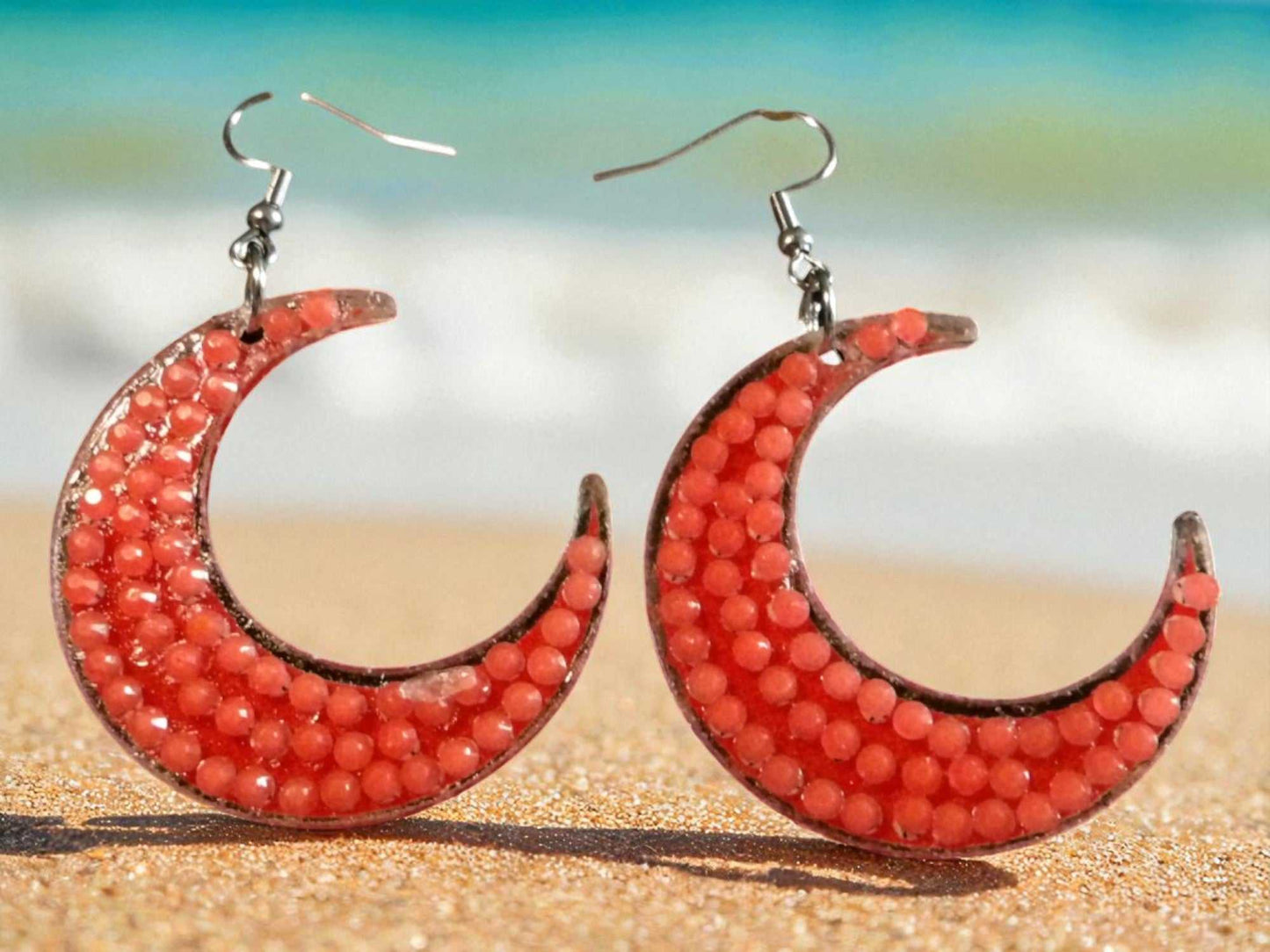 Glow in the dark half moon earrings with orange beads on beach background