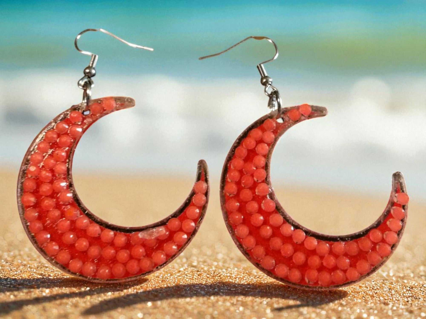Glow in the dark half moon earrings with orange beads on beach background
