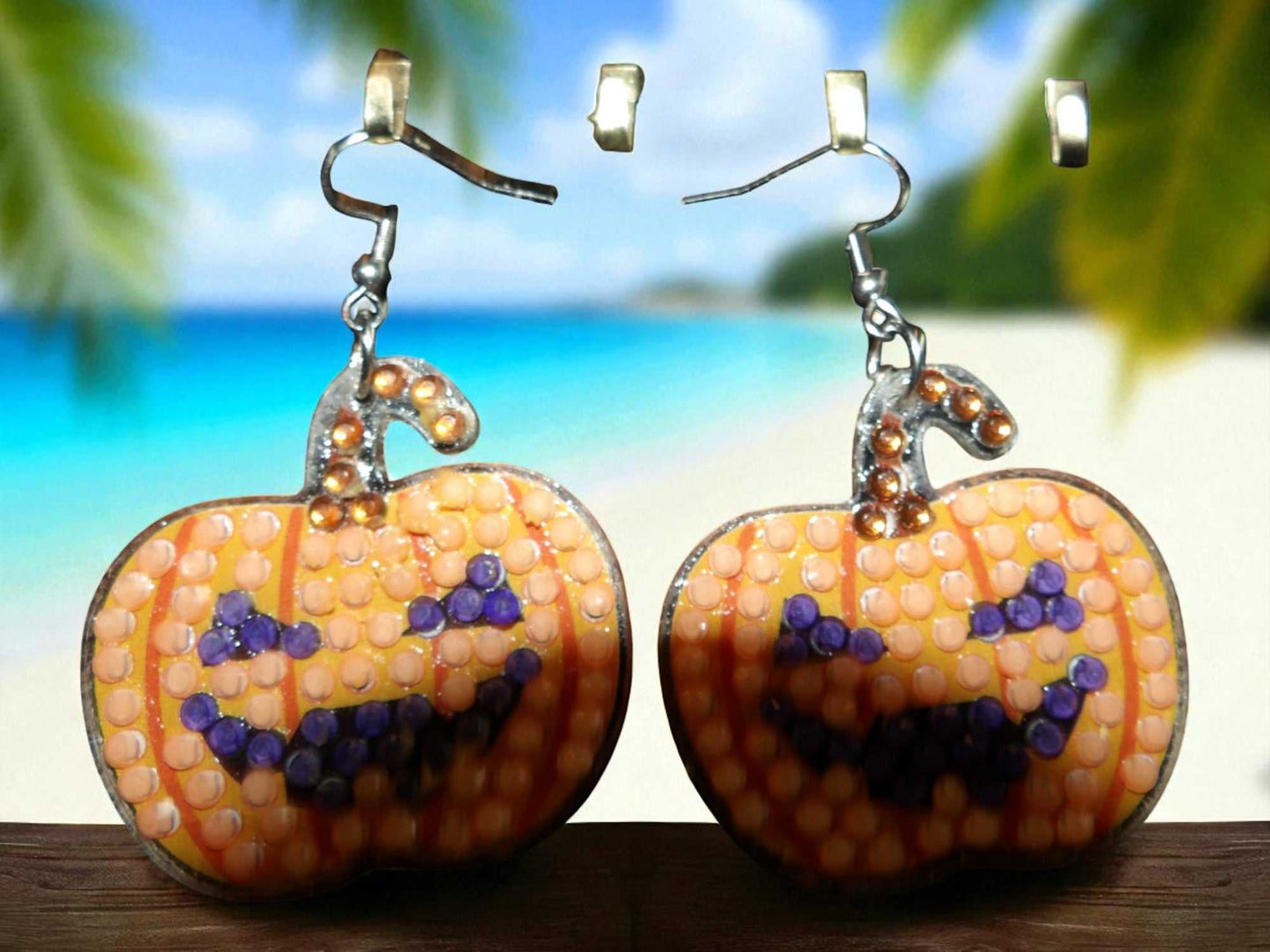 Glow in the dark pumpkin earrings with a spooky jack-o'-lantern design on a beach background