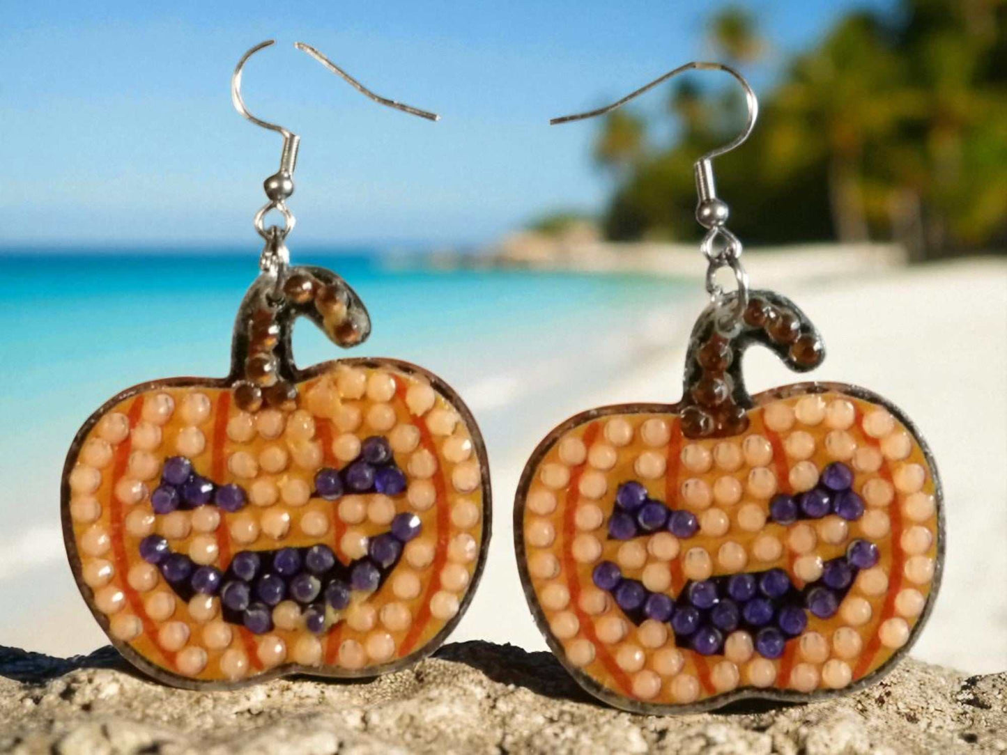 Glow in the dark pumpkin earrings with beaded jack-o'-lantern design on sandy beach background