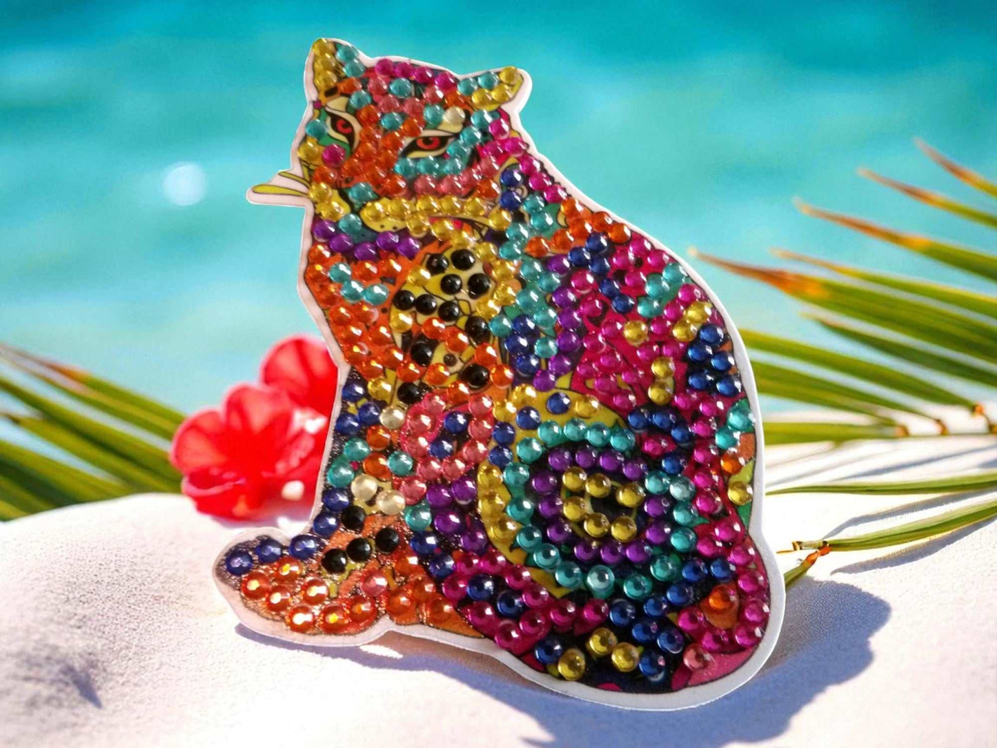 Colorful cougar-shaped magnet decorated with vibrant beads and rhinestones placed on a white surface with tropical background
