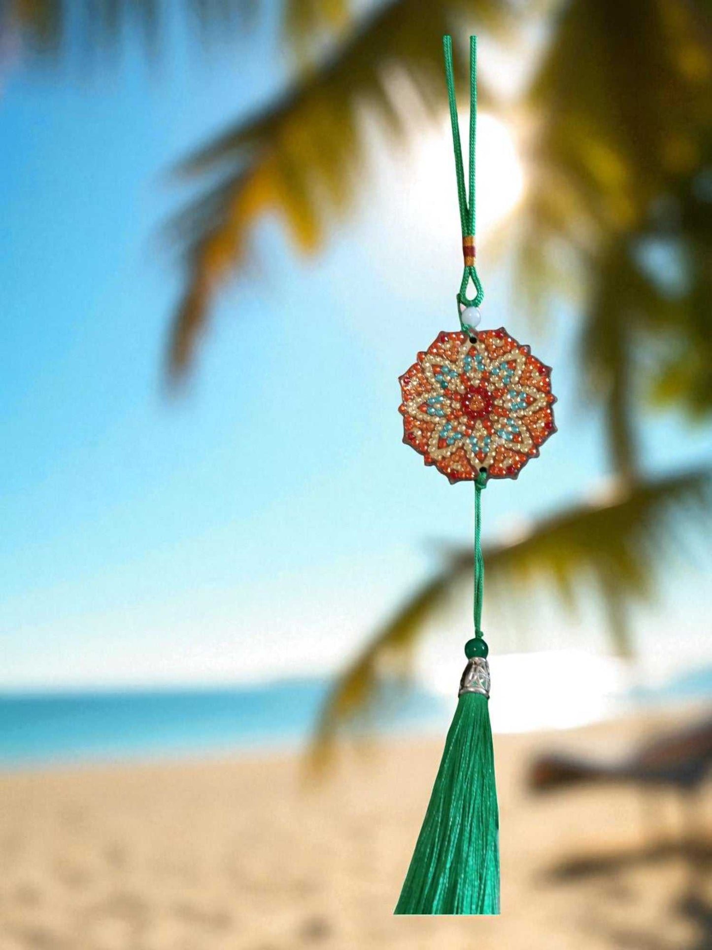 Green red design car ornament hanging with tassel against a tropical beach background