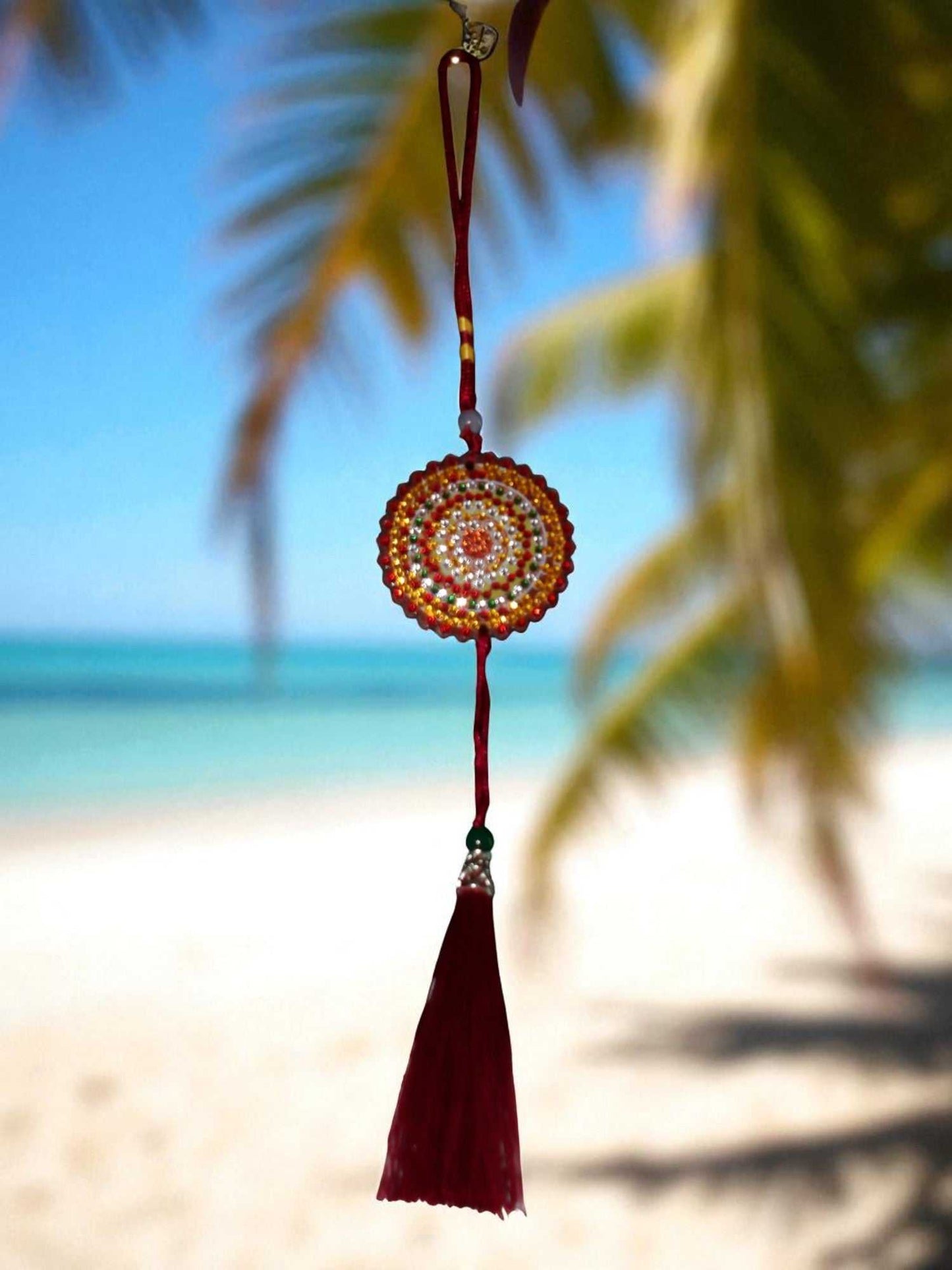 Deep red colorful design car ornament with tassel hanging against beach background