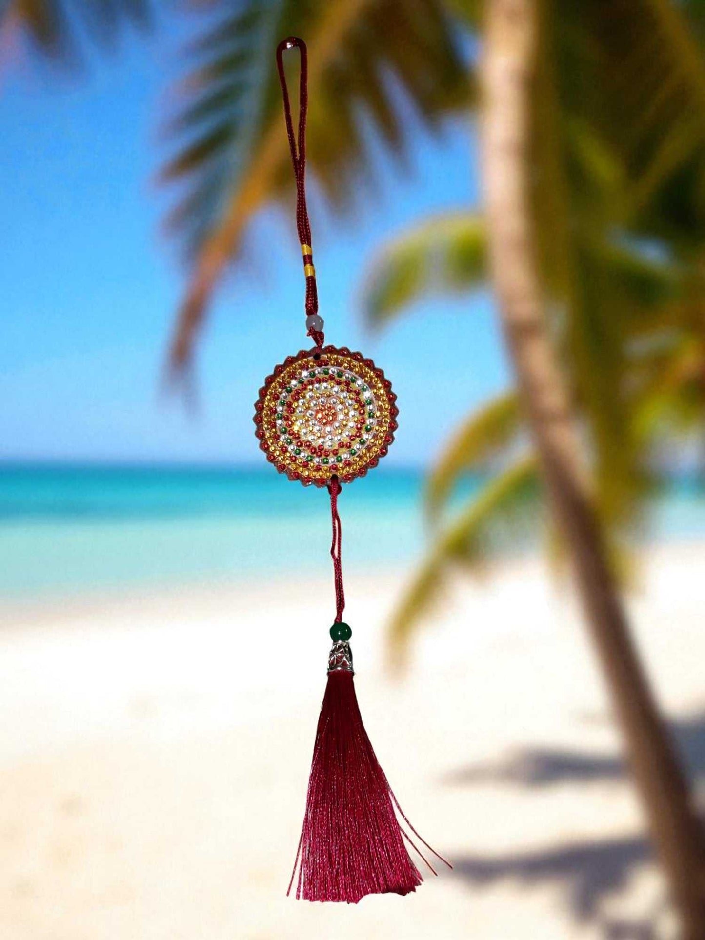 Deep red colorful design hanging car ornament with tassel against a beach background