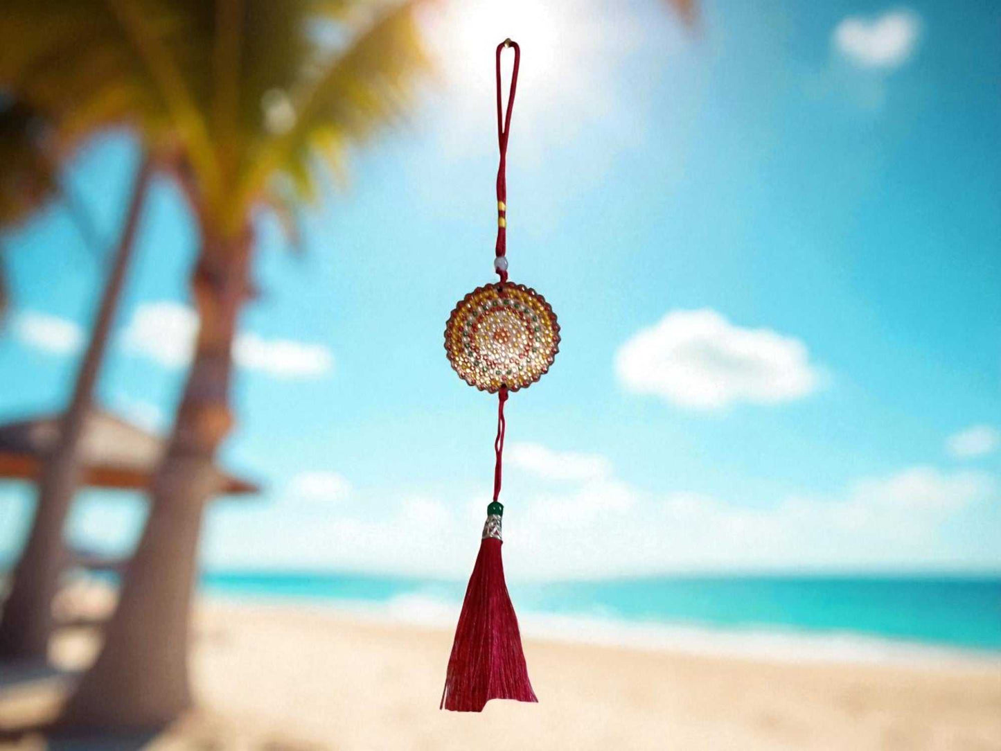 Deep red colorful design car ornament with tassel hanging against blurred beach background