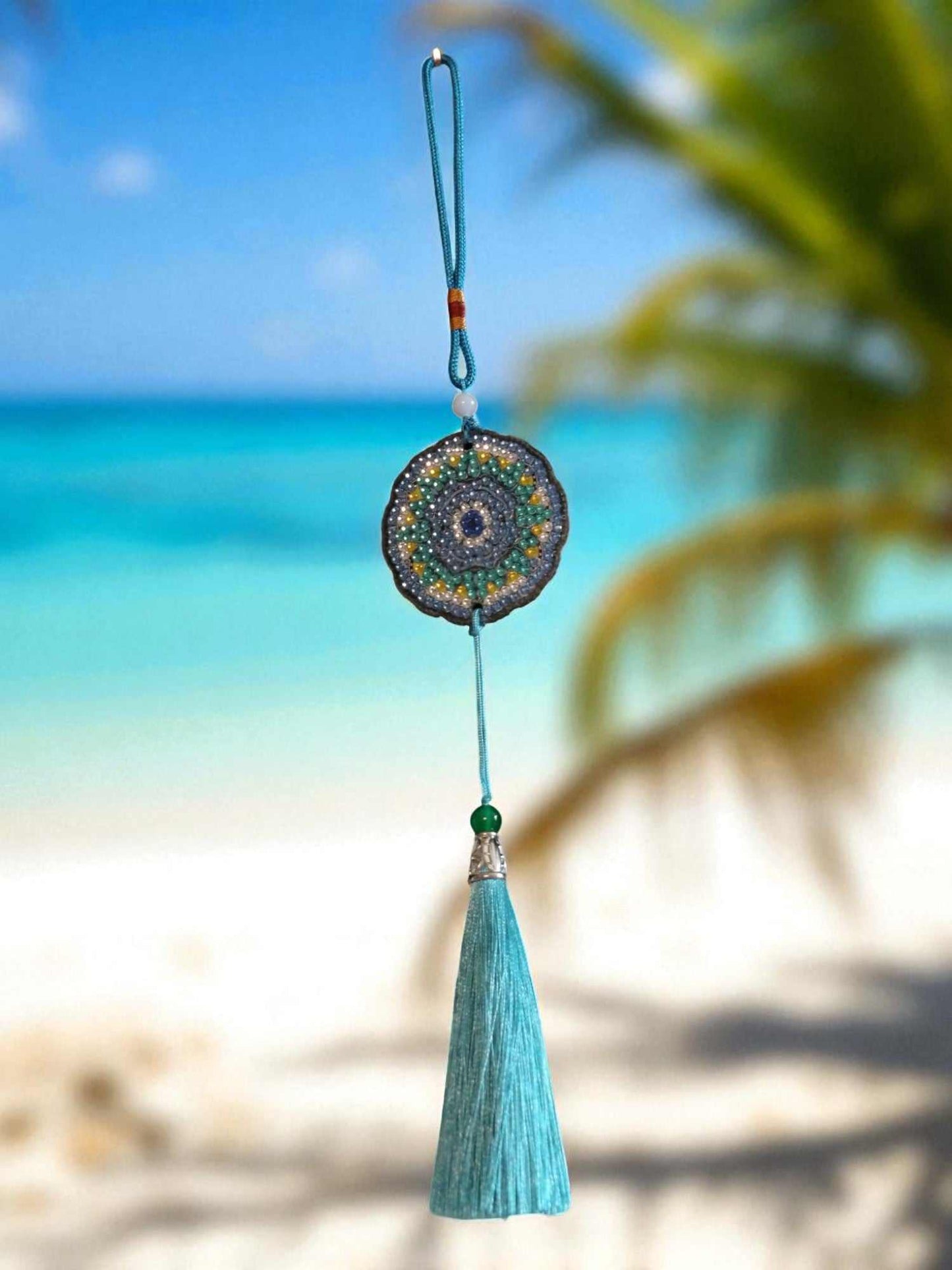 Sky blue colorful car ornament with tassel hanging against beach background