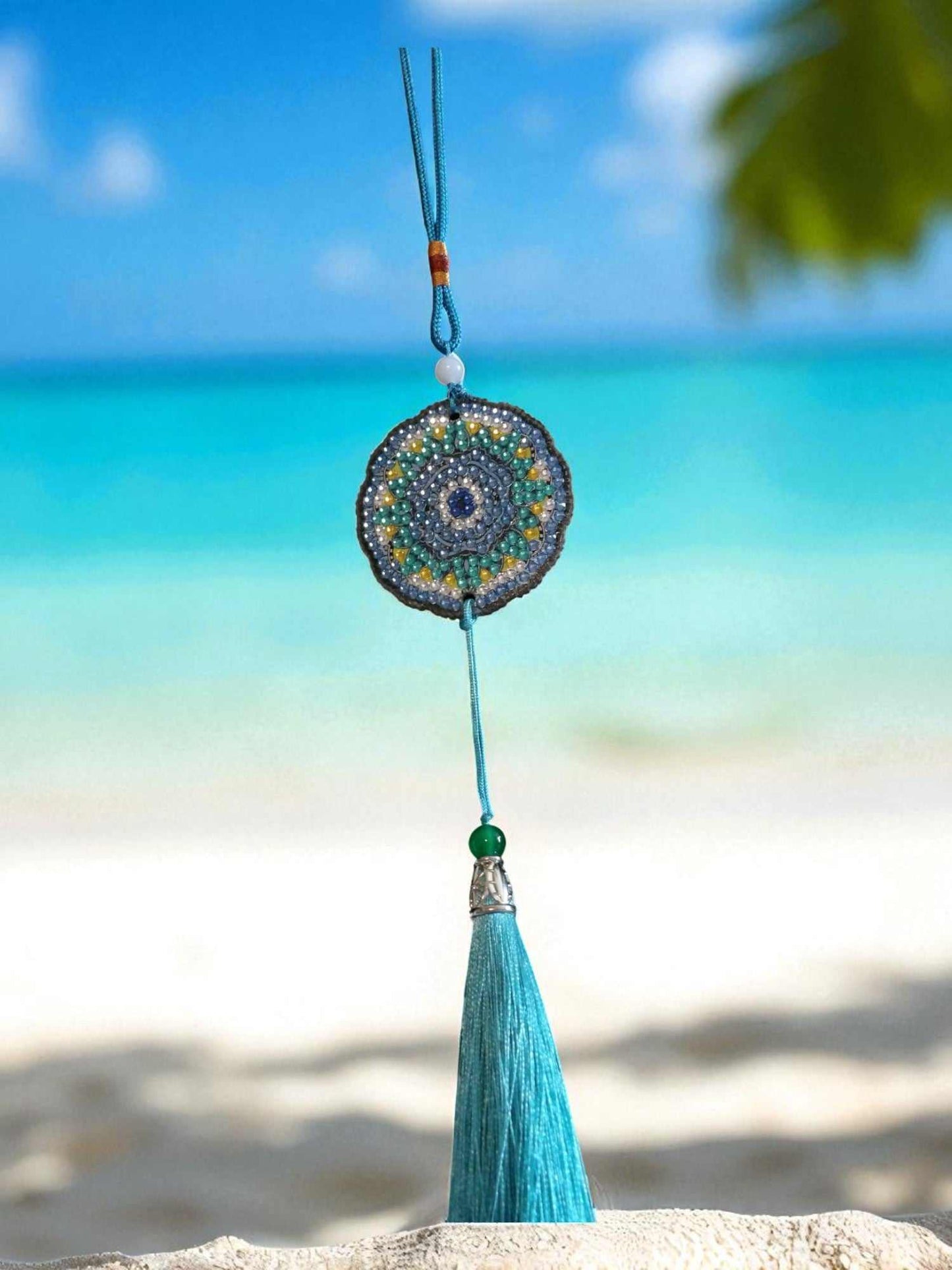 Sky blue colorful car ornament with tassel hanging against beach background
