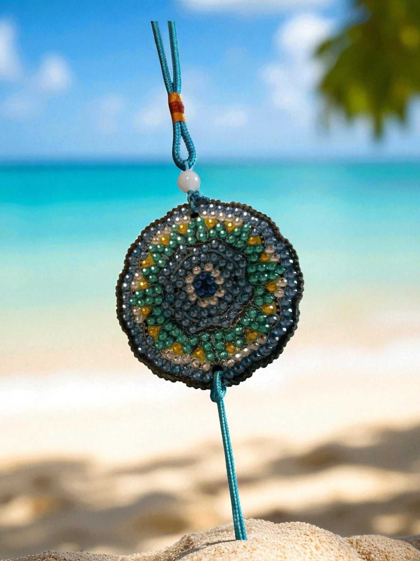 Sky blue colorful beaded car ornament hanging on turquoise string with beach background
