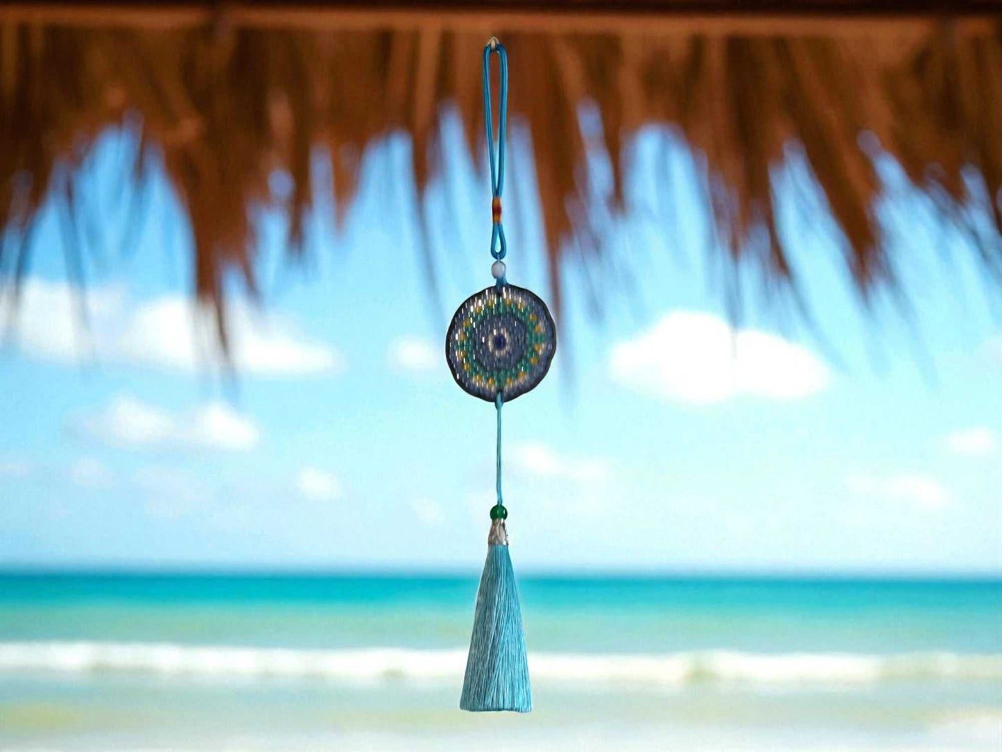 Sky blue colorful car ornament hanging with tassel and beads by rearview mirror against ocean background
