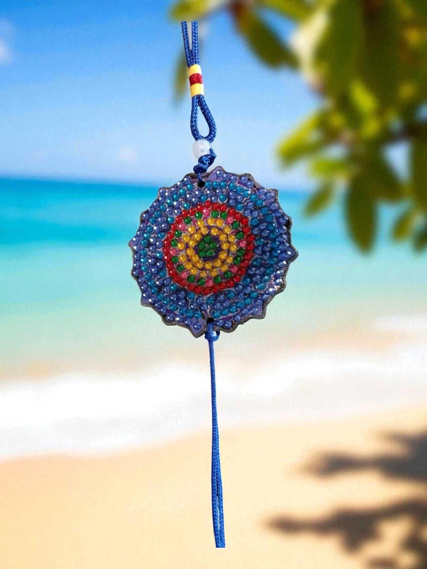 Dark blue colorful design car ornament hanging with vibrant bead pattern against beach background