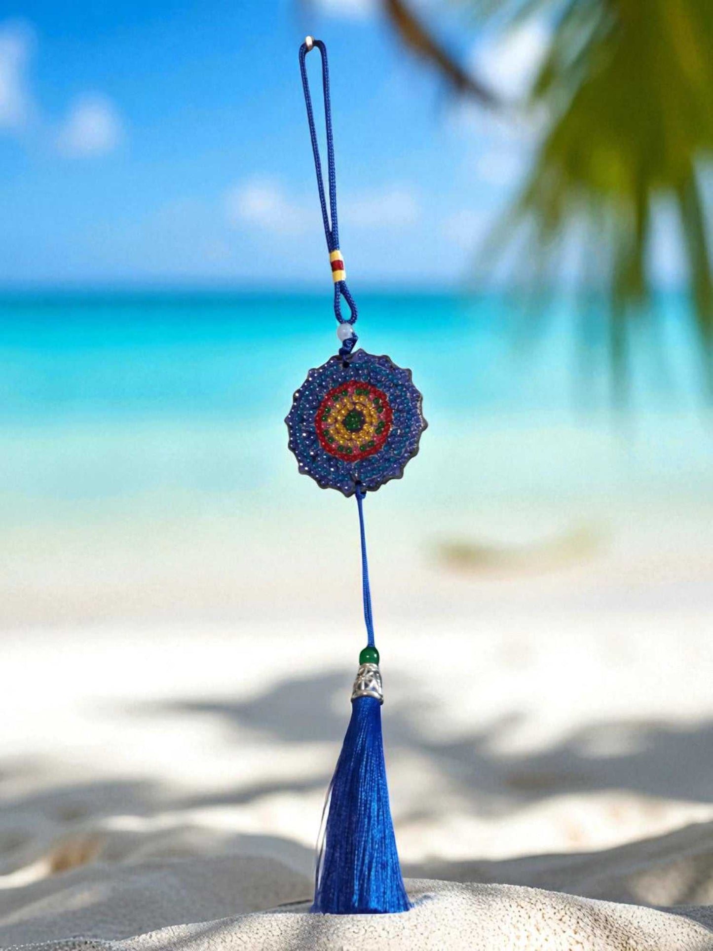 Dark blue colorful design car ornament with tassel hanging on beach background