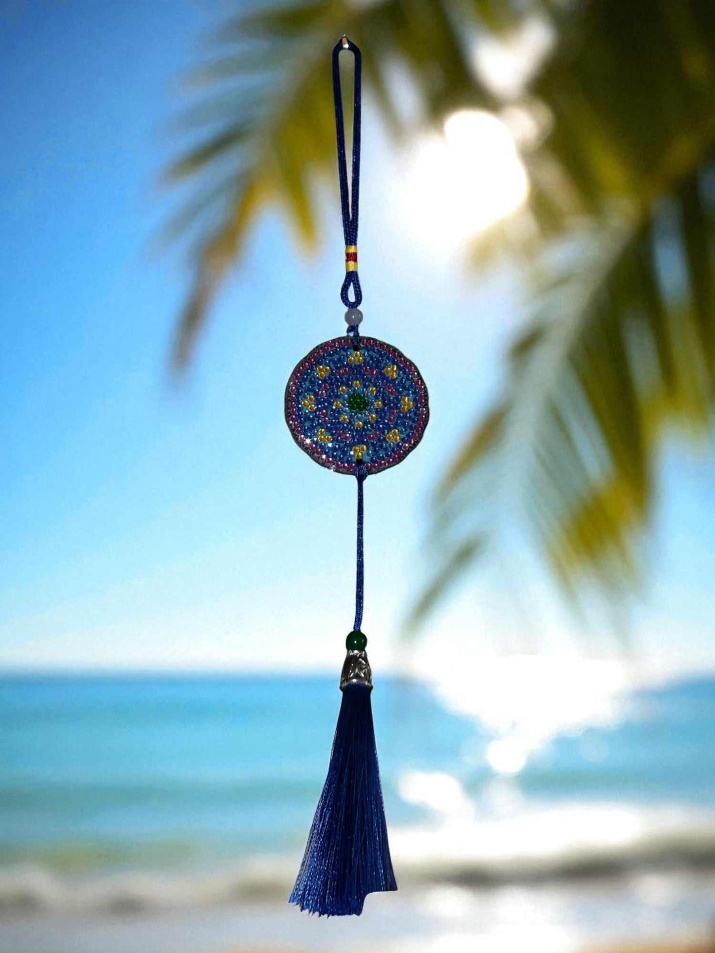 Blue and yellow colorful design car ornament hanging with tassel against a beach background