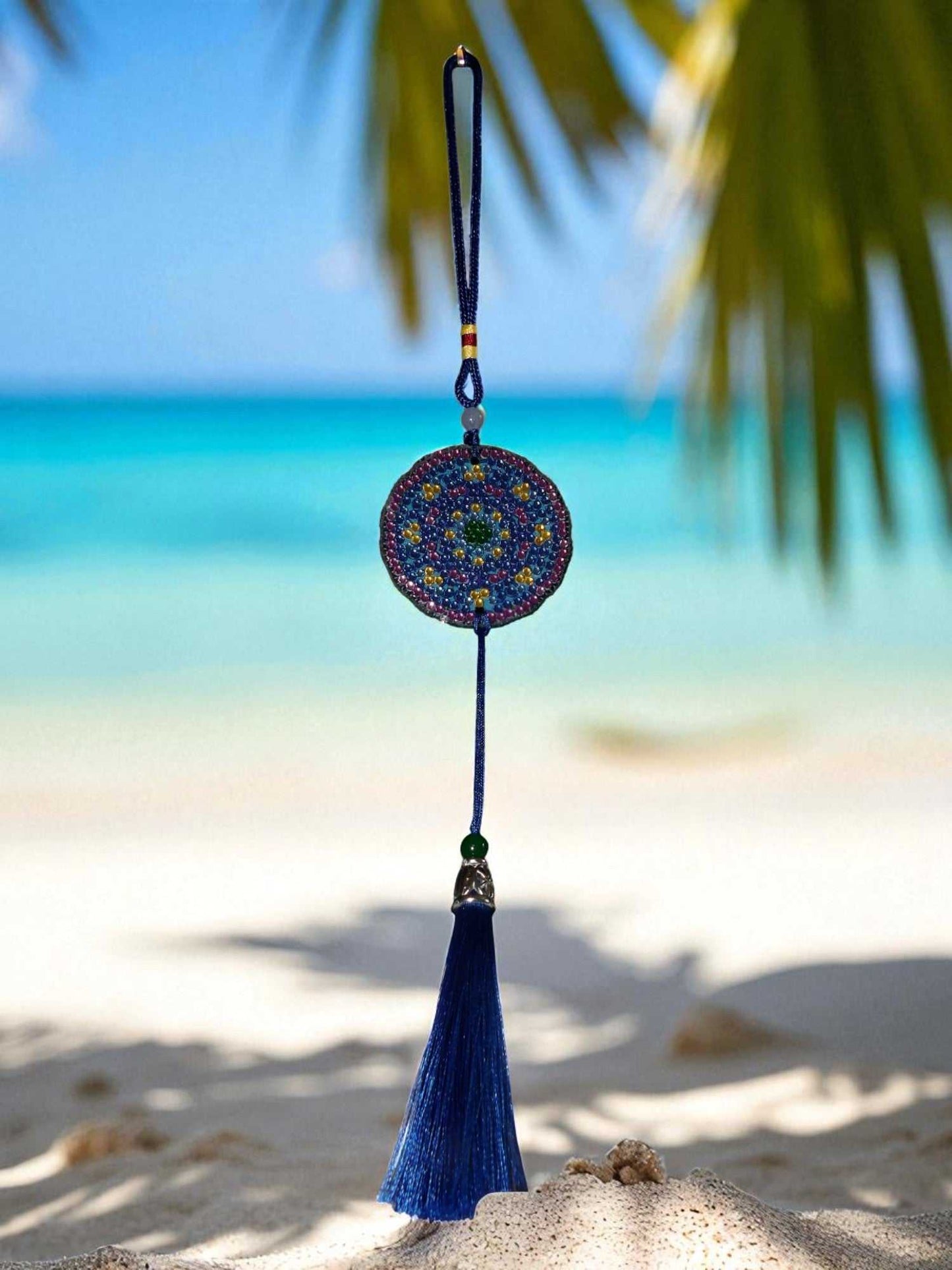 Blue and yellow colorful design car ornament hanging with tassel against beach background