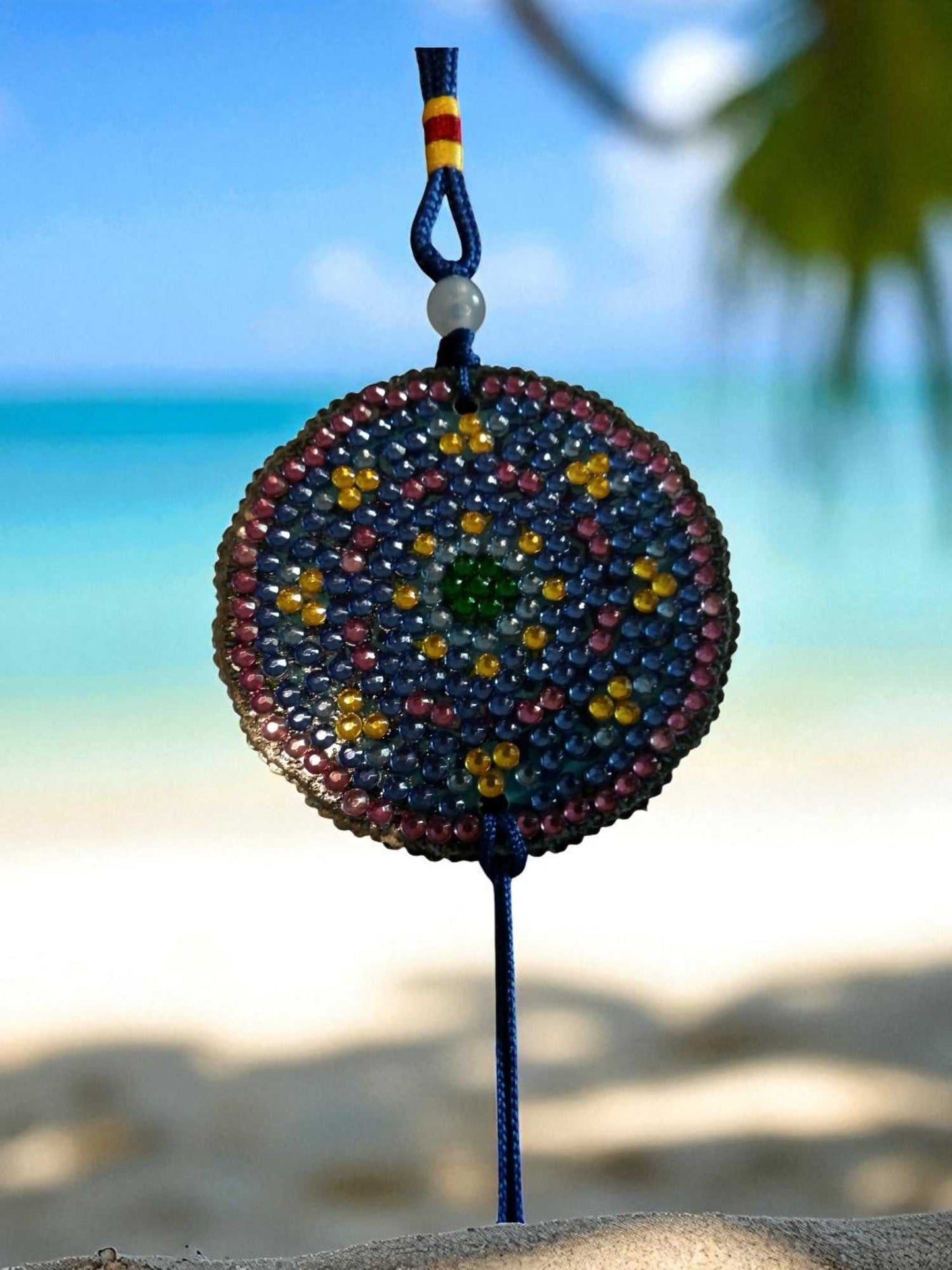 Blue and yellow colorful beaded car ornament hanging with ocean background