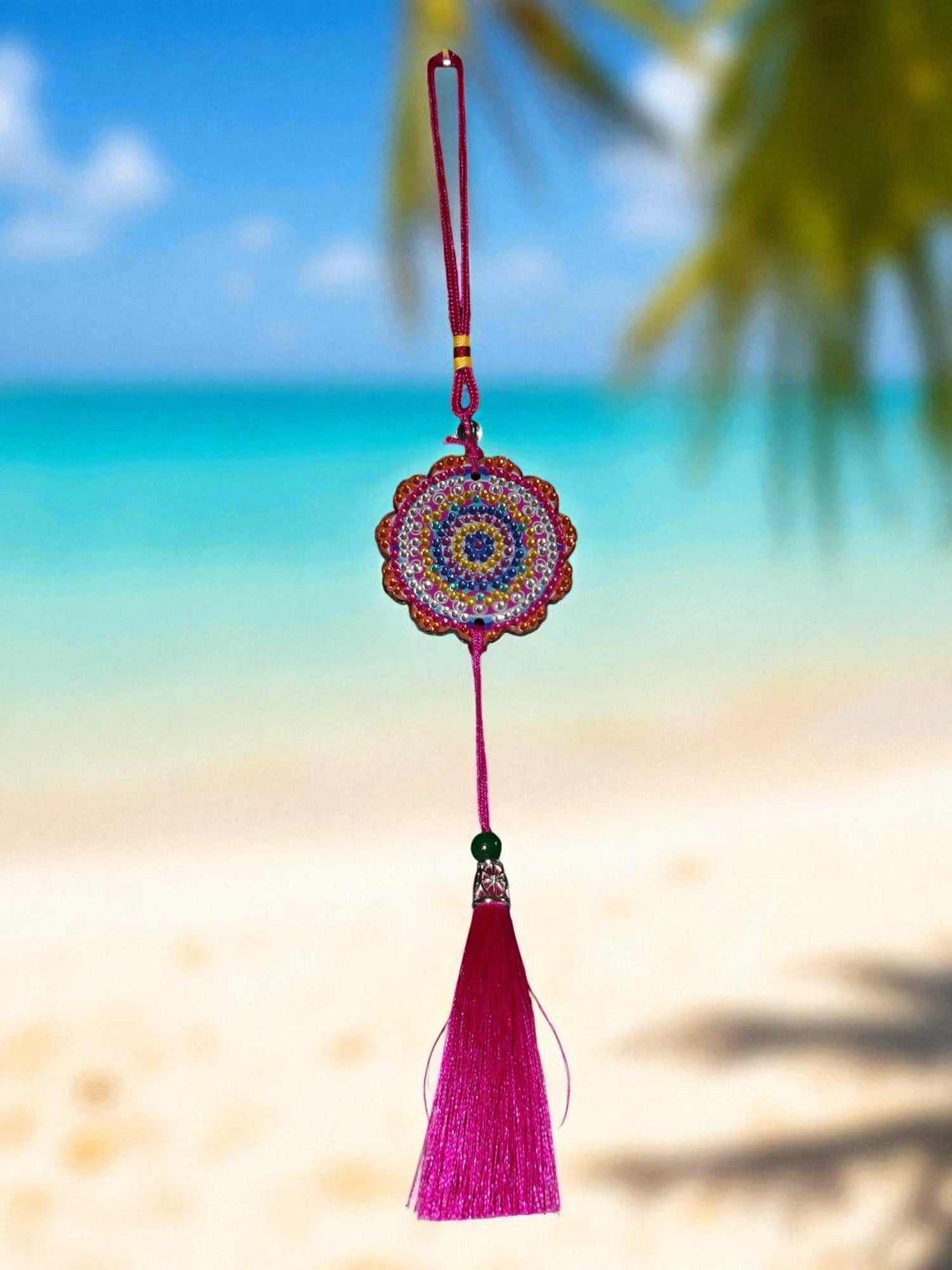 Pink colorful design car ornament with tassel hanging against a beach background