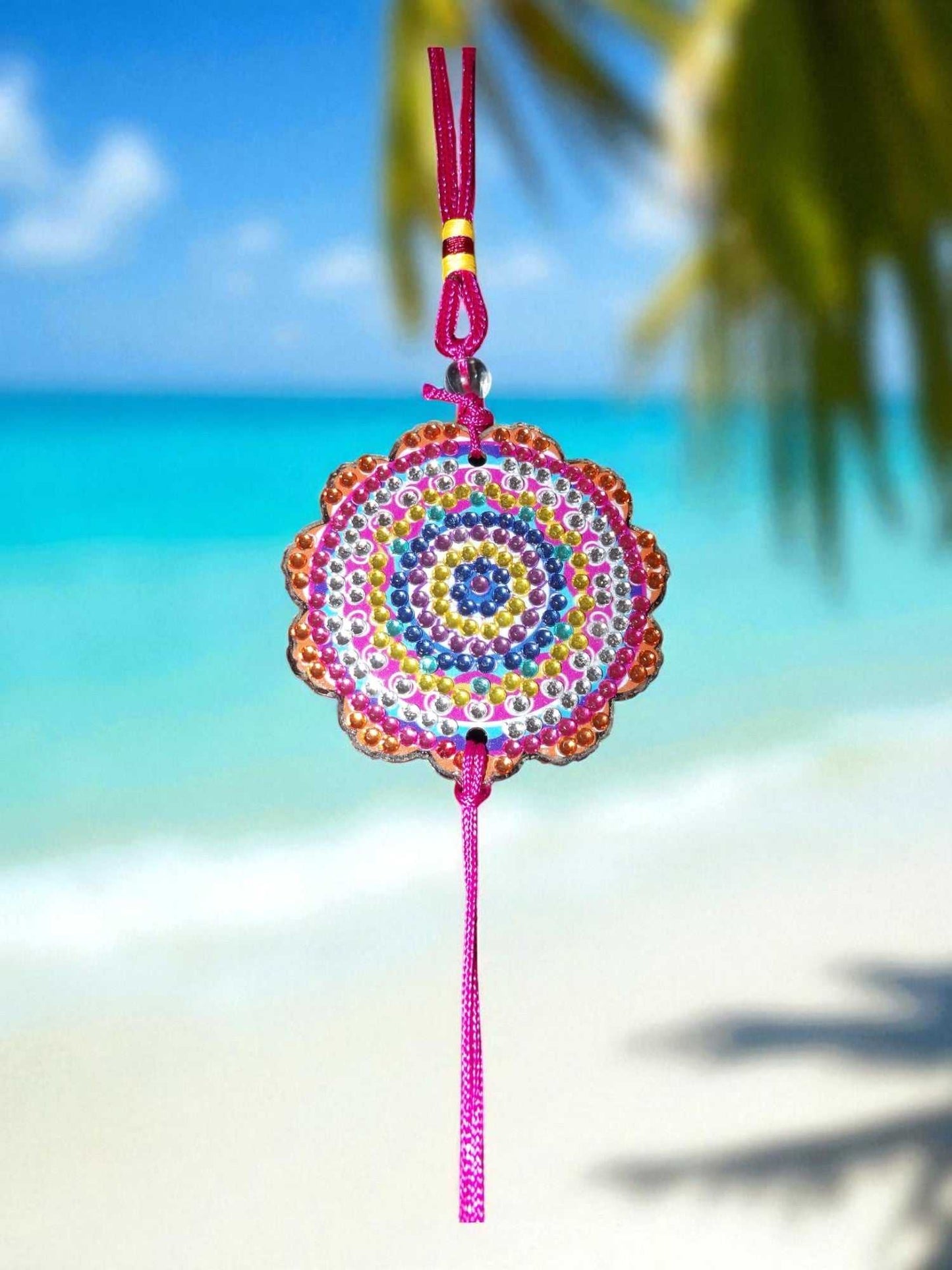 Pink colorful design car ornament with vibrant beadwork hanging against a beach background