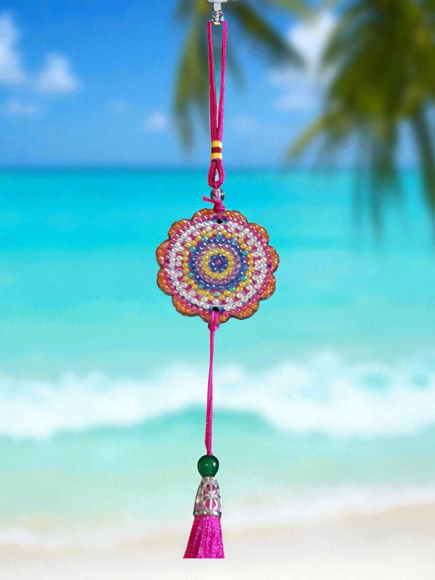Pink colorful design car ornament hanging with beaded circular pattern and tassel against a beach background