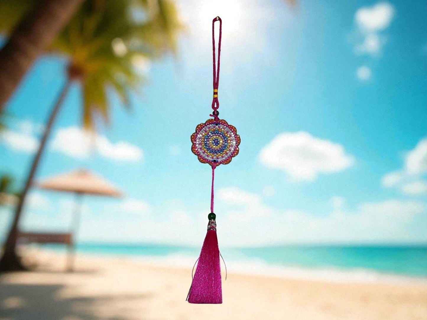 Pink colorful design car ornament hanging with beaded circular pattern and tassel against beach background