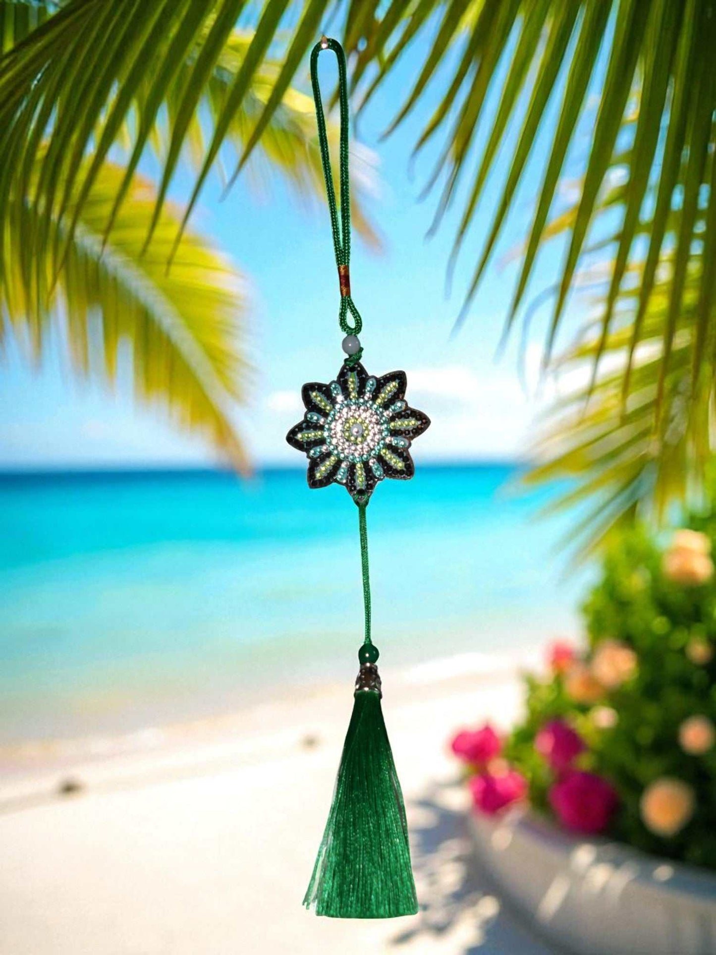 car ornament with beaded flower design and green tassel hanging against tropical beach background