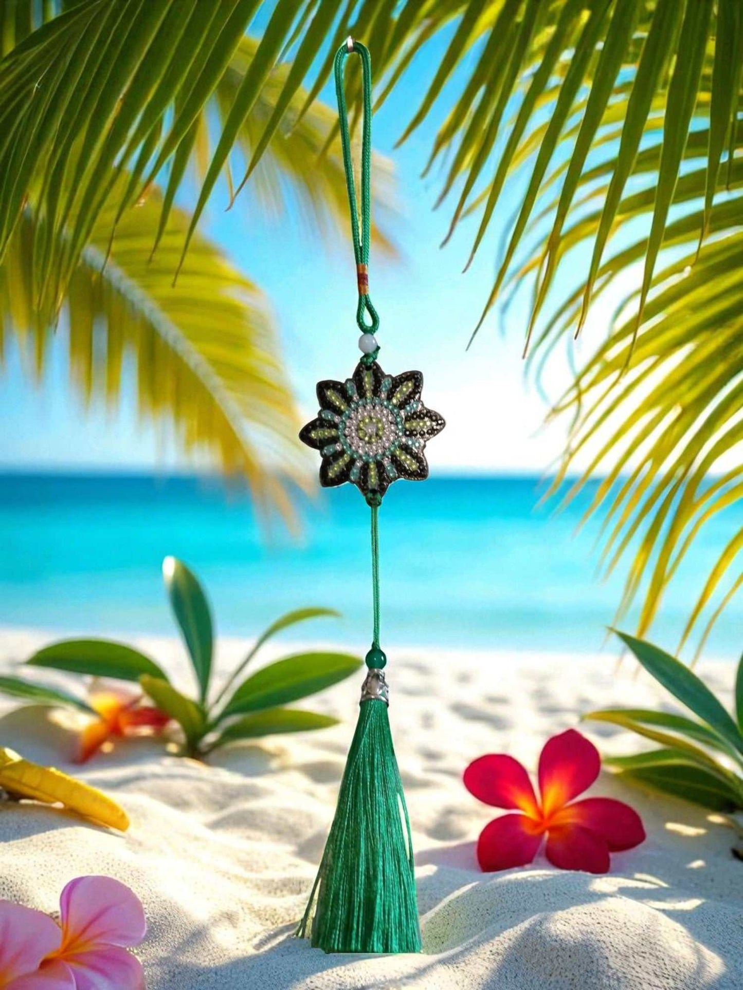 Colocar ornament with beaded flower design and green tassel hanging against tropical beach background