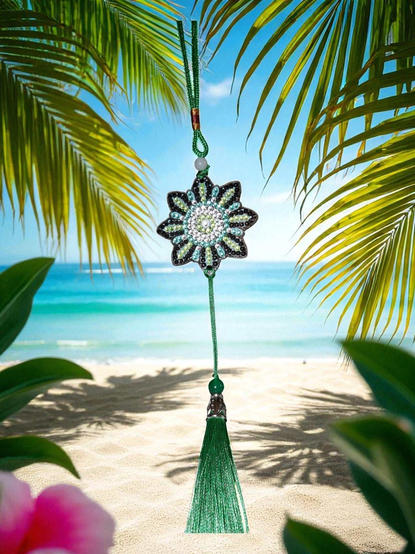 car ornament with beaded flower design and green tassel hanging against tropical beach background