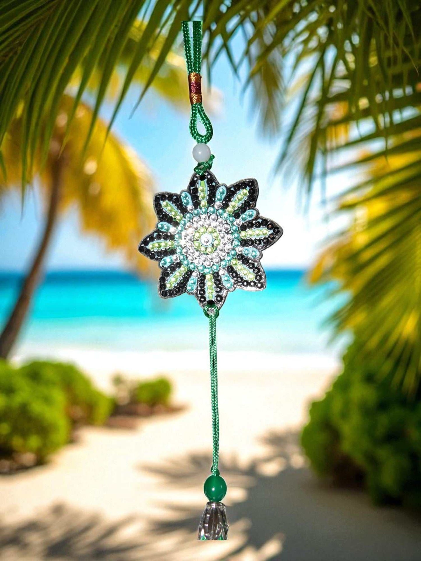 car ornament with beaded flower design and green tassel hanging against tropical beach background