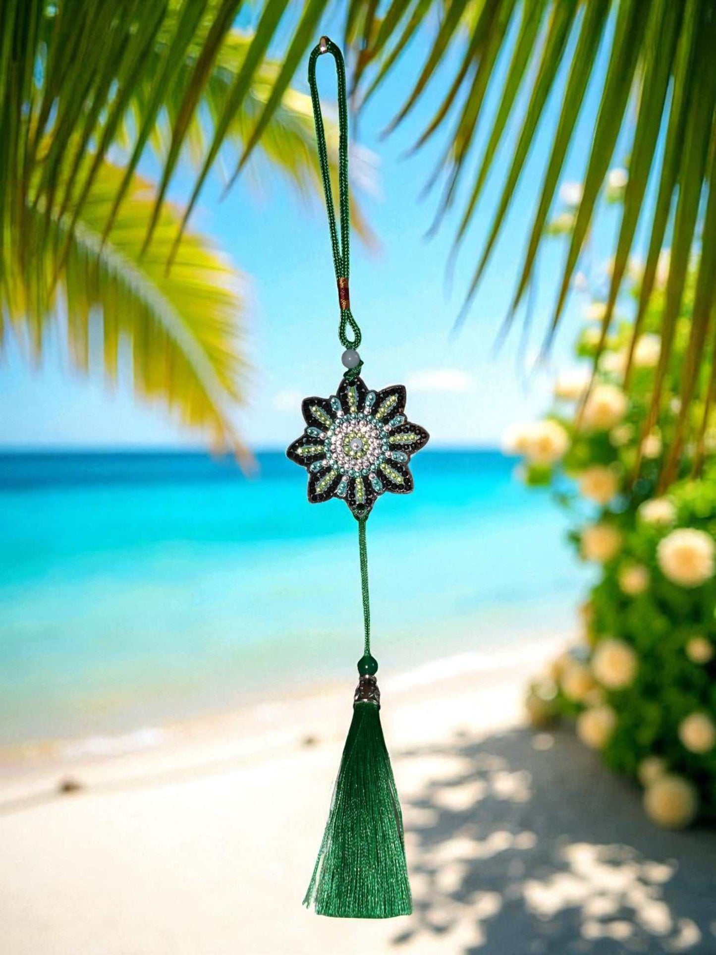 car ornament with beaded flower design and green tassel hanging against tropical beach background