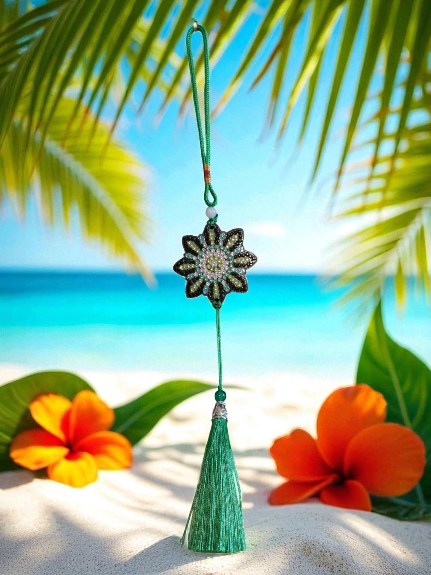 car ornament with beaded flower design and green tassel hanging against tropical beach background