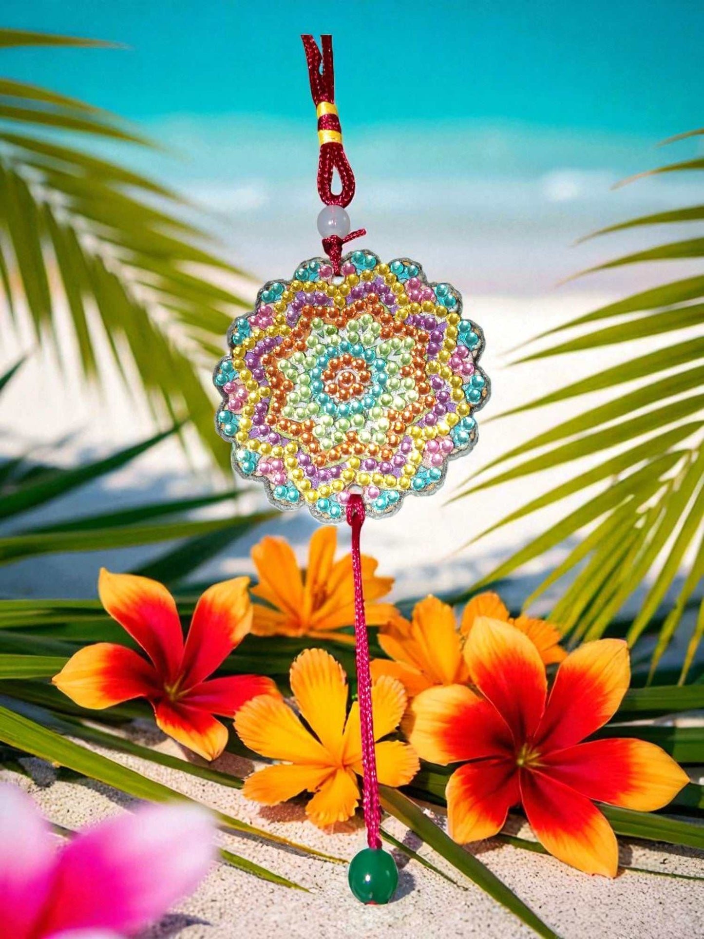 Pink Blue Yellow colorful design car ornament hanging from red string with tropical flowers and leaves background