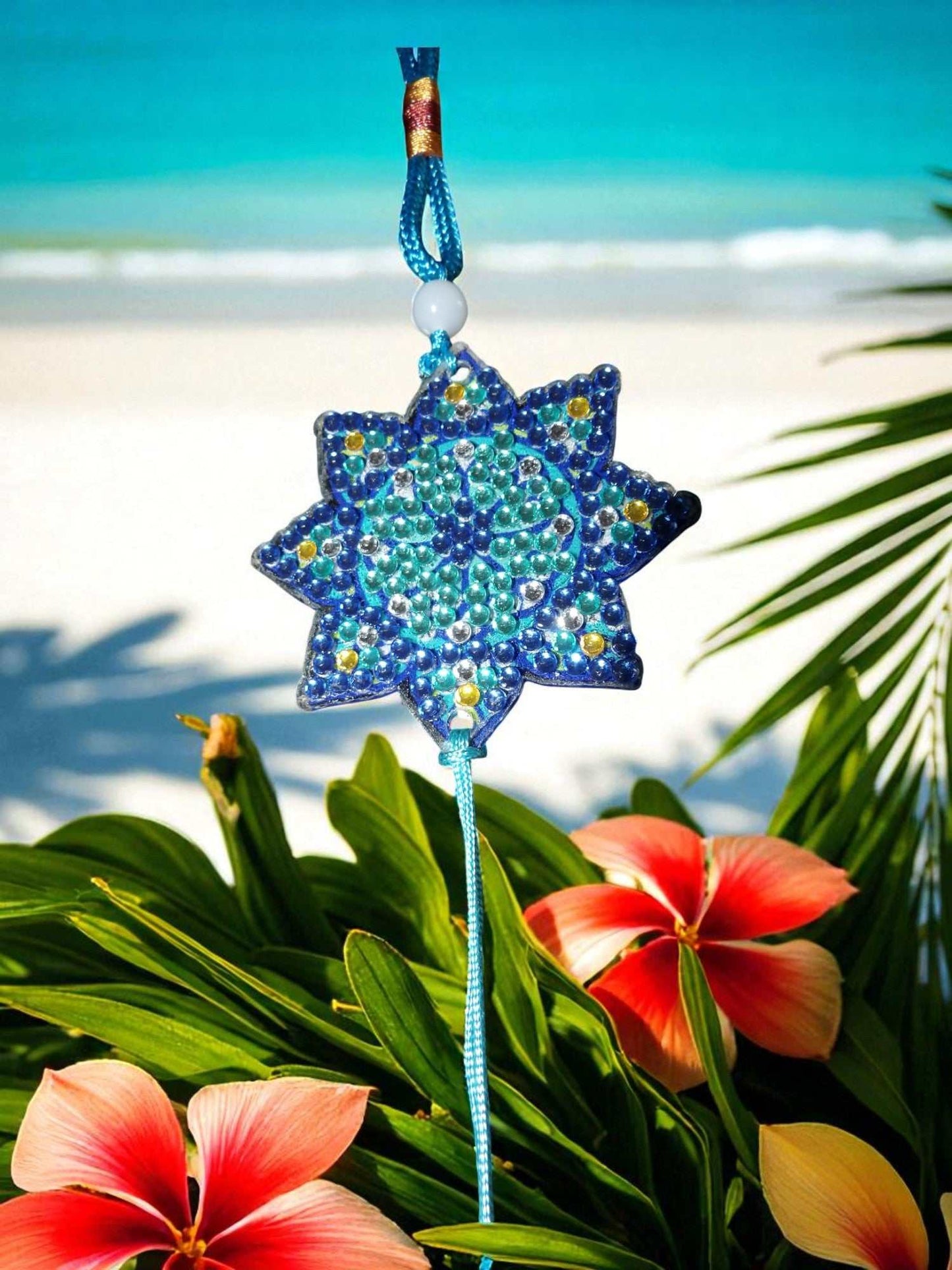 Light Blue Star colorful beaded car ornaments hanging with tropical flowers and beach background