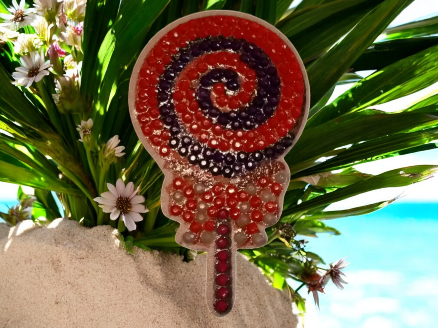 Glow in the dark colorful swirly lollipop magnet on blue surface with greenery accents