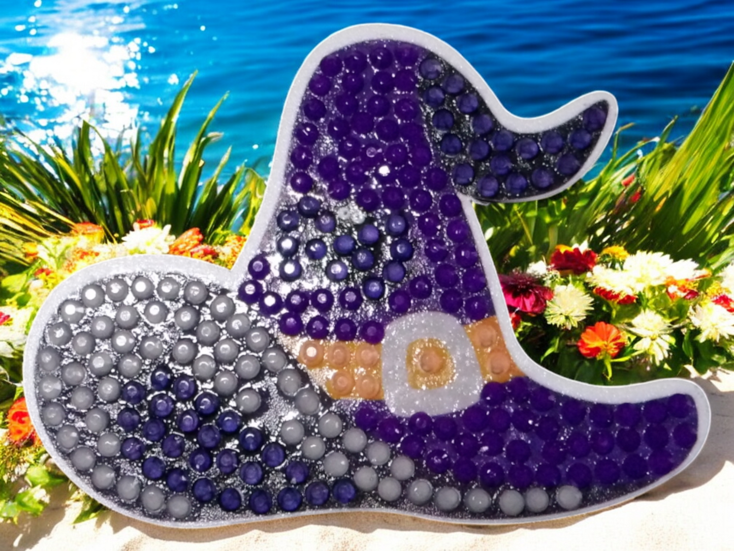 Glow in the dark purple-blue witches hat magnet with sparkling details on beach background