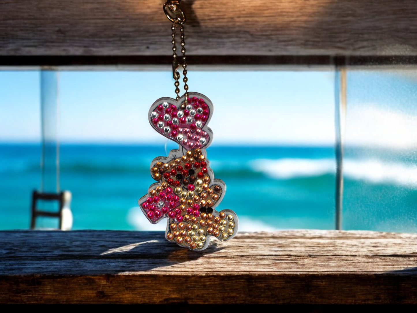Teddy bear keychain decorated with colorful rhinestones hanging by the window with ocean background