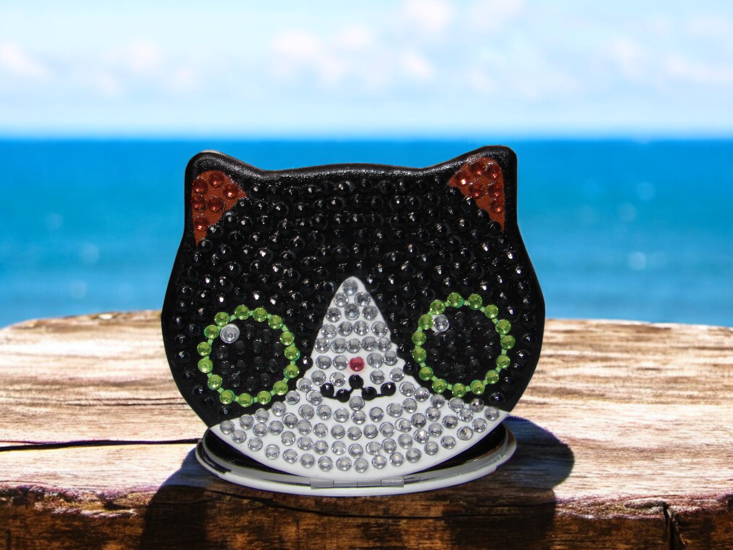 Black and white cat face pocket mirror with magnification and regular side on wooden surface by the sea