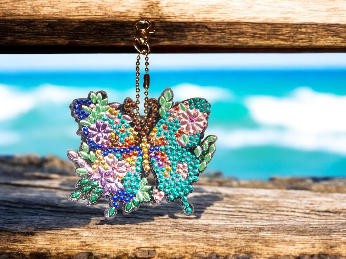 Blue colorful butterfly keychain with floral design hanging on wooden surface by the sea