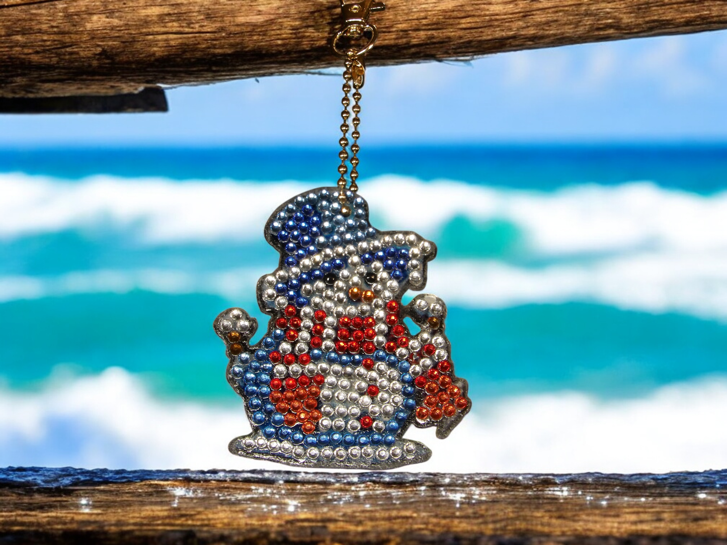 Dark blue hat and red scarf snowman keychain hanging on wooden beam with ocean background