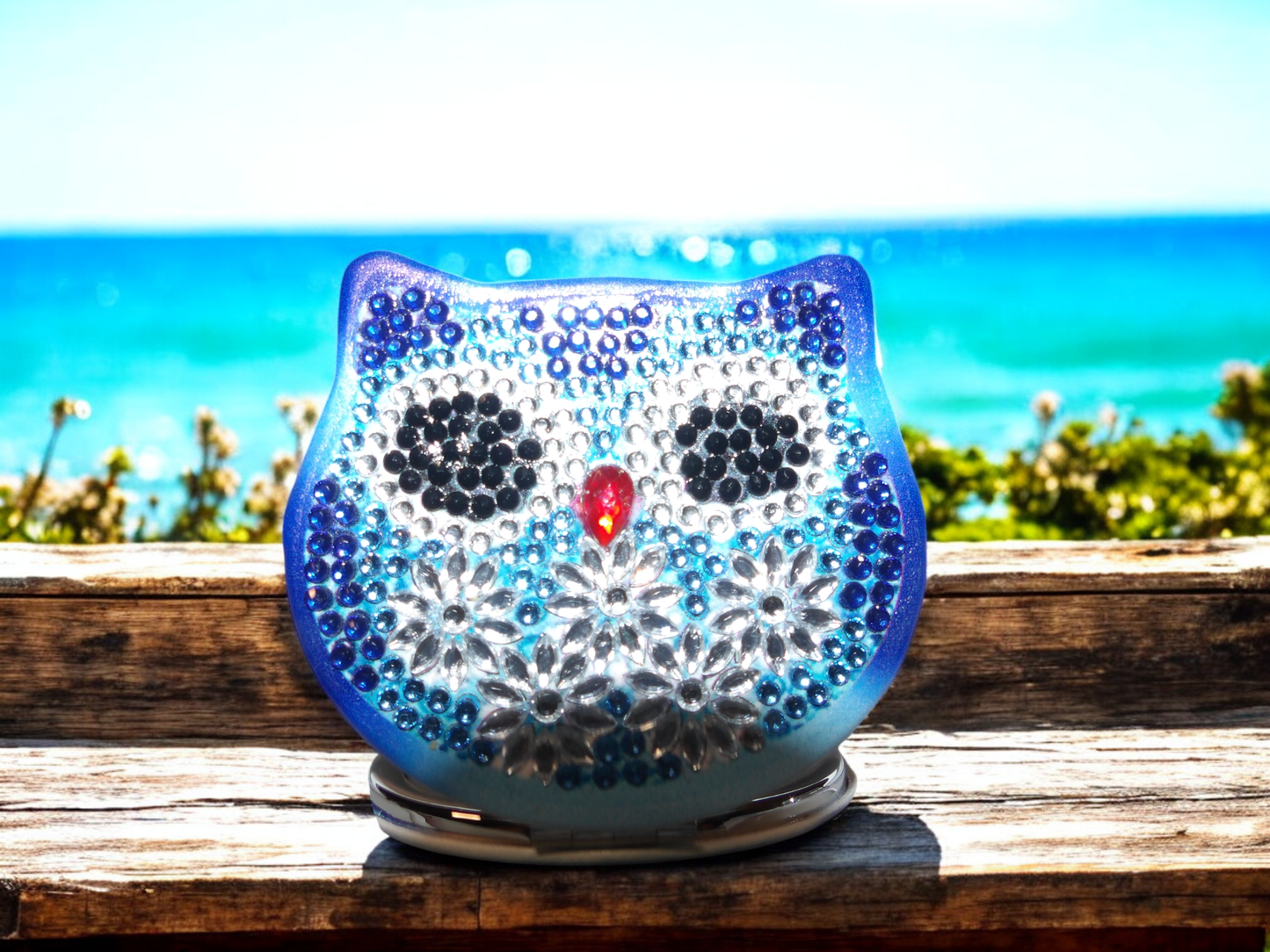 Blue Owl Pocket Mirror with mandala design and magnification on one side displayed outdoors by the sea